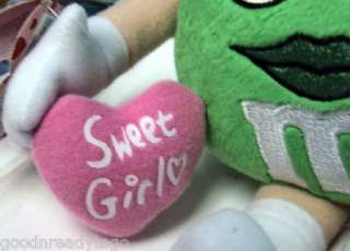 MS. GREEN M&M IS HOLDING A HEART SHAPED PILLOW IMPRINTED WITH SWEET 